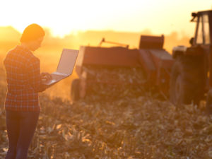 farm machinery and a woman in a field using laptop computer