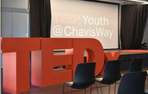 TEDx letters in a large room with a large screen in the background.